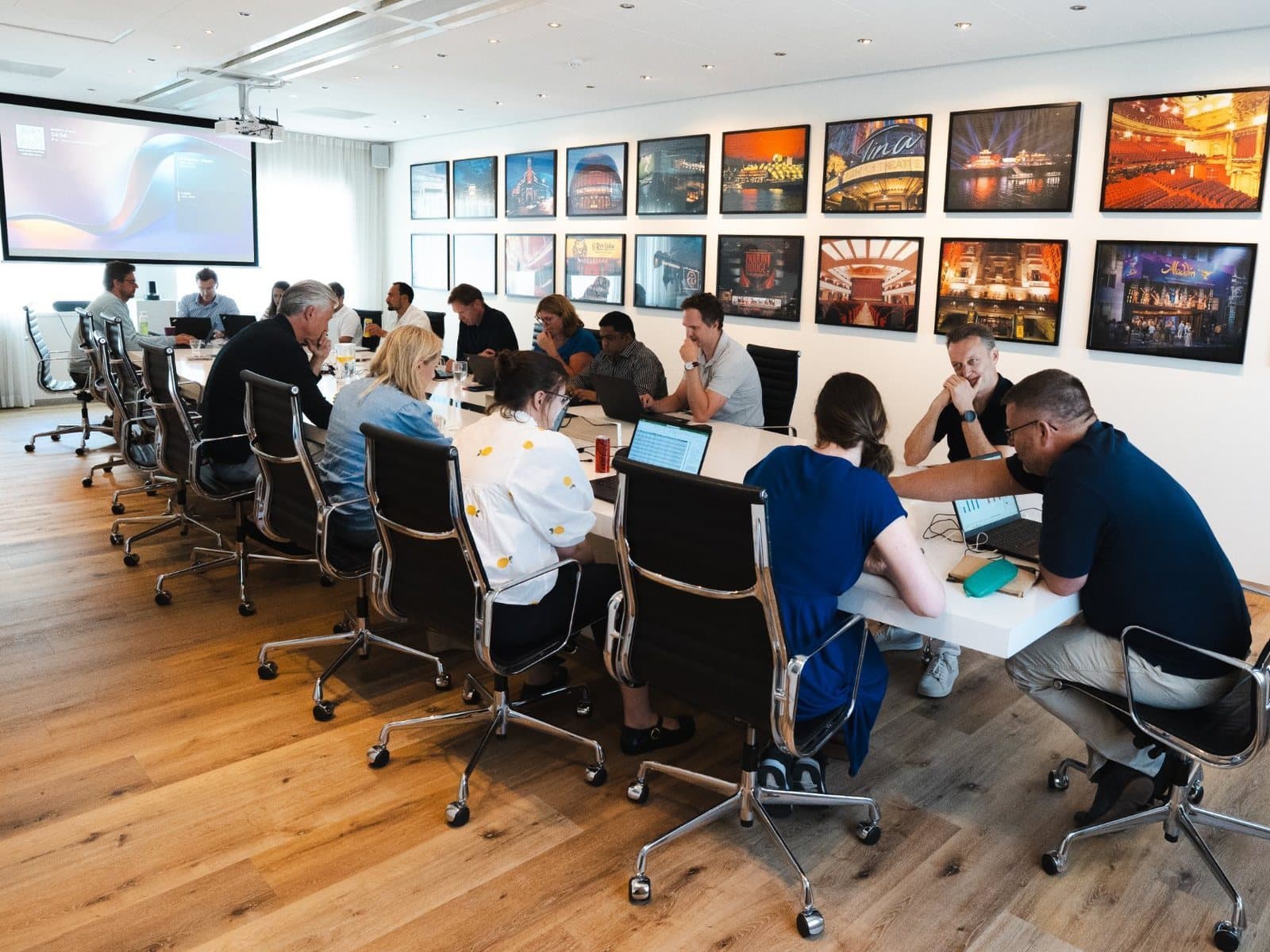 Een grote groep medewerkers werkt aan een lange tafel met laptops aan hun eigen taken