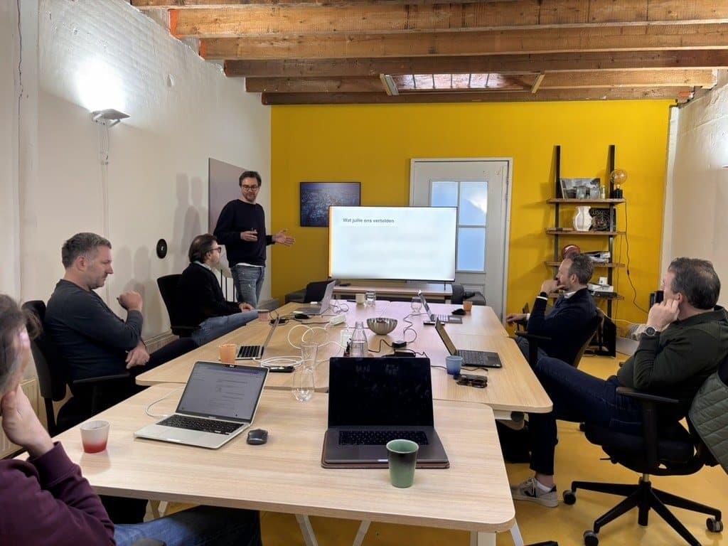 Een team rond de tafel tijdens een werksessie, met een presentatie op het scherm